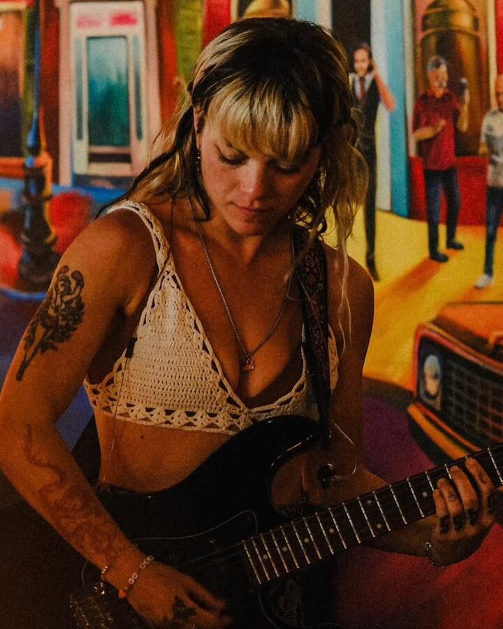 Yara playing guitar live against a colourful mural